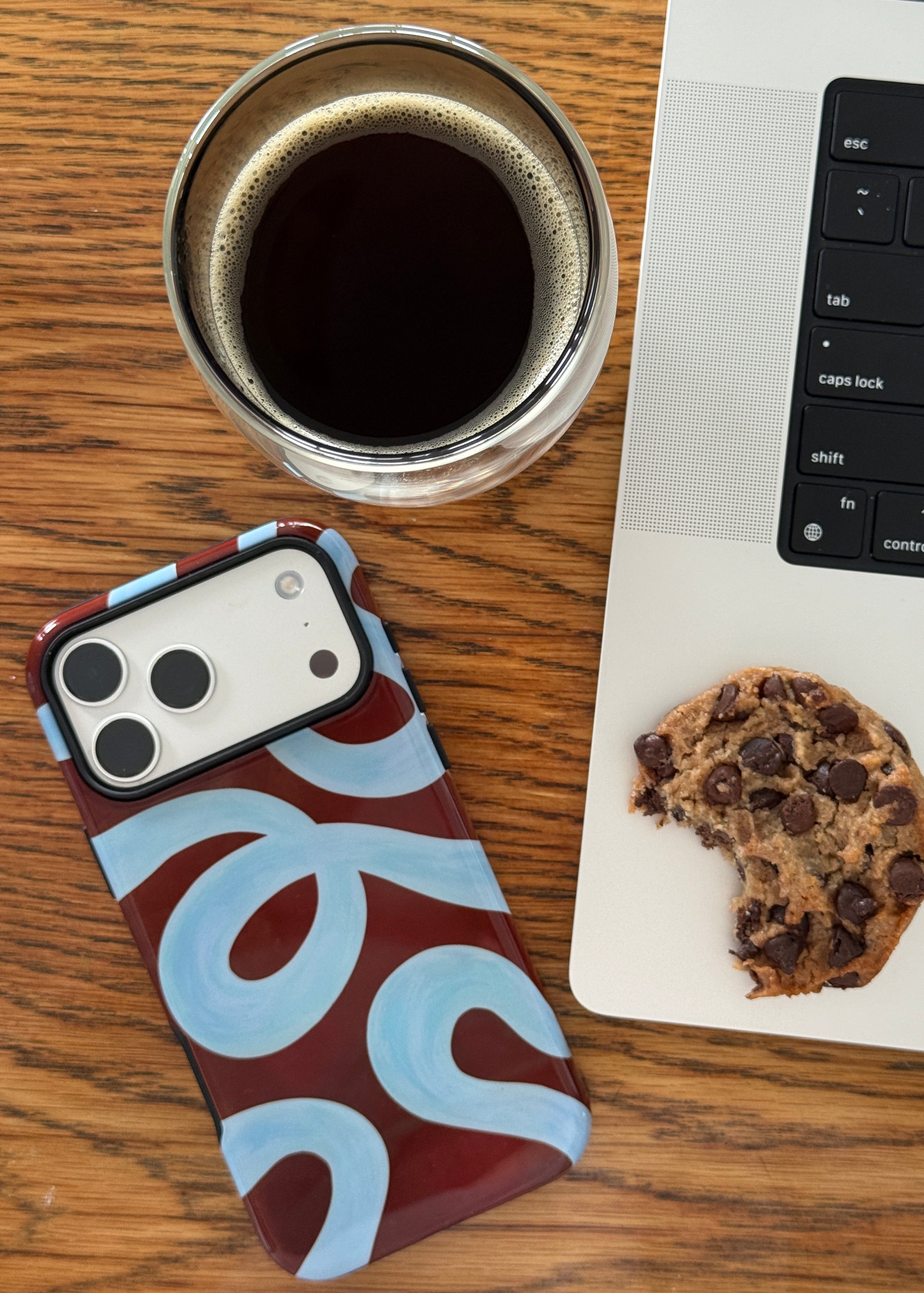 Laptop with a cookie, coffee cup, and cute phone case on a wooden surface